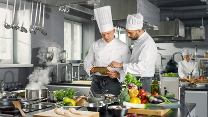 Two Famous Chefs Discuss Their Video Blog while Using Tablet Computer. They Work on a Big Restaurant Stainless Steel Professional Kitchen. © Gorodenkoff