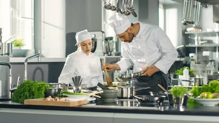 Photo sur Plexiglas Cuisinier Le célèbre chef et son apprentie préparent un plat spécial dans la cuisine d& 39 un restaurant cinq étoiles moderne.