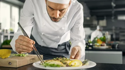 Crédence de cuisine en verre imprimé Cuisinier Le célèbre chef décore son plat de poisson spécial avec quelques légumes verts. Il travaille dans une cuisine moderne.