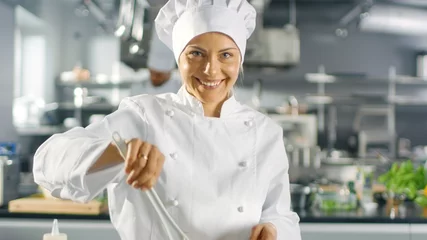 Selbstklebende Fototapete Kochen In einem berühmten Restaurant bereitet Köchin Salat zu und lächelt in eine Kamera. Sie arbeitet in einer großen modernen Küche.