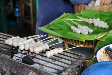 Pork ball with wood stick grilling on the metal grill grate in the stove, raw Pork ball prepare on the banana leaf. Thai lifestyle food in the market.