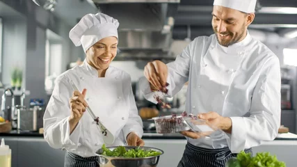 Photo sur Aluminium Cuisinier L& 39 équipe de chefs célèbres masculins et féminins préparent une salade pour leur restaurant cinq étoiles. Ils travaillent sur une grande cuisine professionnelle en acier inoxydable de restaurant.
