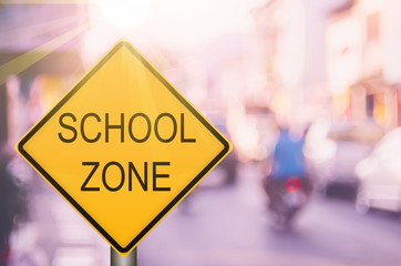 School zone warning sign on blur traffic road with colorful bokeh light abstract background.