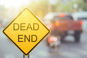 Dead end warning sign on blur traffic road with colorful bokeh light abstract background.