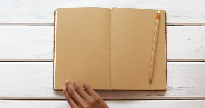 male hand open diary paper 6 brown  page then close  on the white wooden desk, top view and overhead shot use for blank template book mock up to add any text content