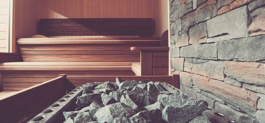 Wooden Bathhouse with a heating pot filled with stones, close up. Wooden sauna interior with equipment.