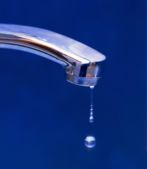 Drops of water dripping from the iron crane on blue background. Concept of rational use of natural resources