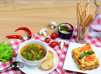 European lunch - vegetables soup, lasagna bolognese and dessert served on a wooden table. Italian food background with a copy space.
