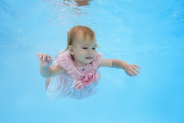 Fototapeta na wymiar A little girl in a pink dress swims under water in the pool