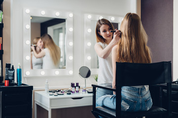 Professional makeup artist working on young girl creating natural look in beauty salon