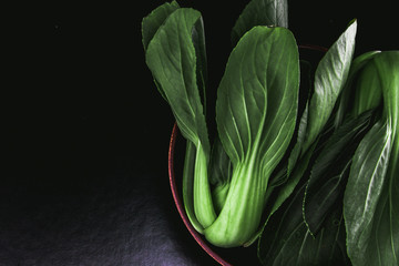 close up Fresh baby green bok choy in bowl on the  black background , overhead or top view shot - obrazy, fototapety, plakaty
