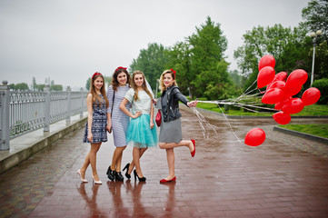 Attractive bride posing with her three lovely bridesmaids with red heart-shaped balloons on the pavement with lake on the background. Bachelorette party.