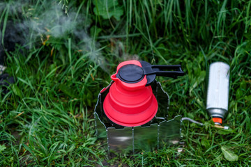 Fodable camping kettle with boiling water standing on burning stove.