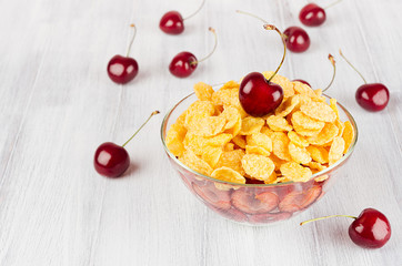 Summer breakfast with golden corn flakes, ripe cherries on white wood board. Decorative border with copy space.