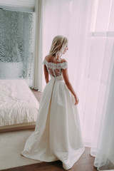 Gorgeous, luxury blonde bride near a window on the background of the stylish room. Morning preparation
