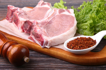 Raw pork steak with spices Leaves lettuce on wooden cutting board. Ready for cooking.