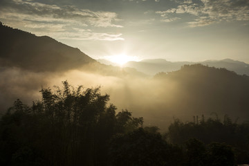 Obraz premium Morning sun rays through the fog over mountain slopes.