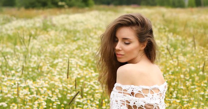 Young beautiful brunette girl posing against a background of a camomile glade
