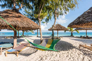 handmade wooden chaise longues, straw umbrellas and hammock on a beach near ocean