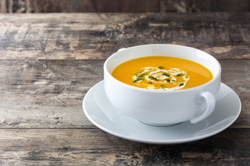 Pumpkin soup in white bowl on wooden table
