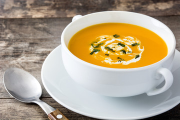 Pumpkin soup in white bowl on wooden table
