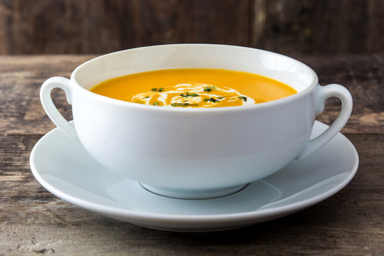 Pumpkin soup in white bowl on wooden table
