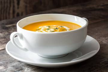 Pumpkin soup in white bowl on wooden table
