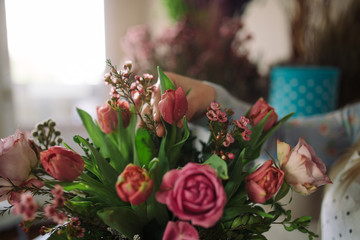 woman florist making bouquet of flowers indoor. Female florist preparing bouquet with roses, tulip in flower shop. Close up