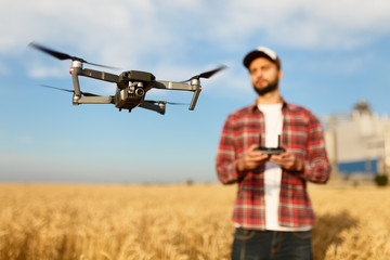 Compact drone hovers in front of farmer with remote controller in his hands. Quadcopter flies near...