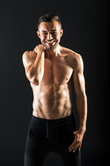 Fototapeta na wymiar Smiling muscular shirtless man against dark background