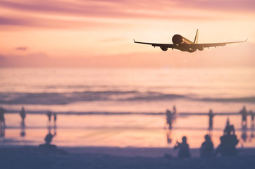 Fototapeta na wymiar Airplane flying over blur people relax on tropical sunset beach with bokeh sun light wave abstract background.