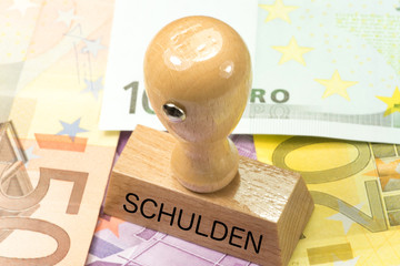 Viele Euro Geldscheine und ein Stempel mit dem Aufdruck Schulden