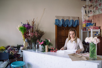 woman florist making bouquet of flowers and cutting off the wrapping paper indoor. Female florist preparing bouquet with  tulip in flower shop.