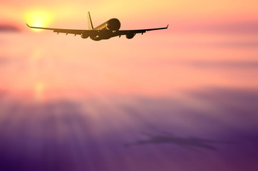 Airplane flying over blur tropical beach with smooth wave and sunset sky abstract background.
