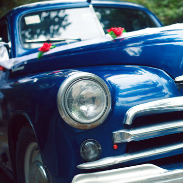 Blue colored vintage wedding car decorated with roses and white ribbon. Mag wheels. Hipster style. Daylight. Close up. Outdoor shot