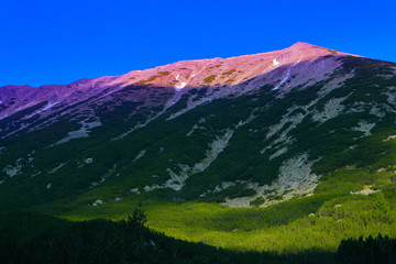 Beautiful view on the high green mountains peaks, on the colorful sunrise sky background. Mountain hiking paradise landscape, no people.