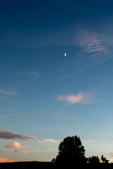 silhouette of a Man sitting on a bench against the sunset with rising moon in the background