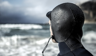 Rear view of surfer wearing wetsuit looking out to sea
