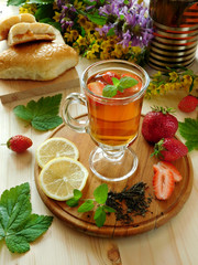 Herbal tea with herbs, lemon and strawberries in a glass for breakfast on a wooden background