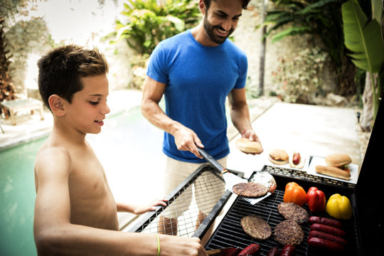 A man and boy standing at a barbecue cooking food.