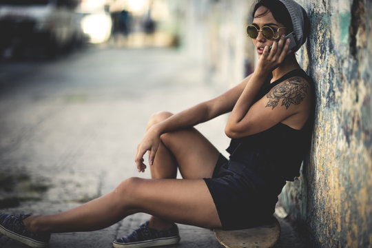 Young woman sitting on a skateboard talking on a cell phone.