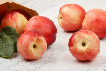 Ripe red peaches in the paper bag on the white wooden table