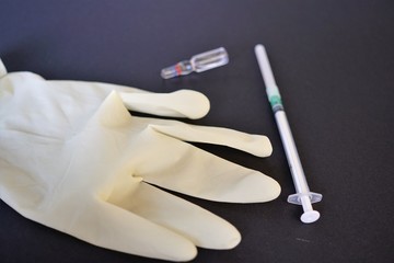 White glove, syringe and glass ampoule on black background