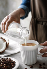Woman pouring coconut milk into cup of coffee on table
