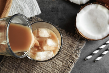 Woman pouring cold coconut coffee into glass with ice cubes on table