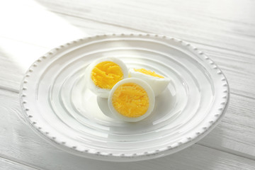 White ceramic plate with sliced hard boiled eggs on wooden table. Nutrition concept