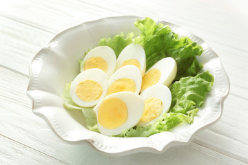 Ceramic plate with sliced hard boiled eggs and lettuce on wooden table. Nutrition concept
