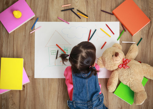 Little Asian girl drawing in paper on floor indoors, top view of child on floor