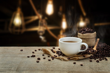 Hot Coffee cup with Coffee beans on the wooden table and the coffee shop background