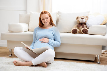 beautiful redhead pregnant woman reading book at home